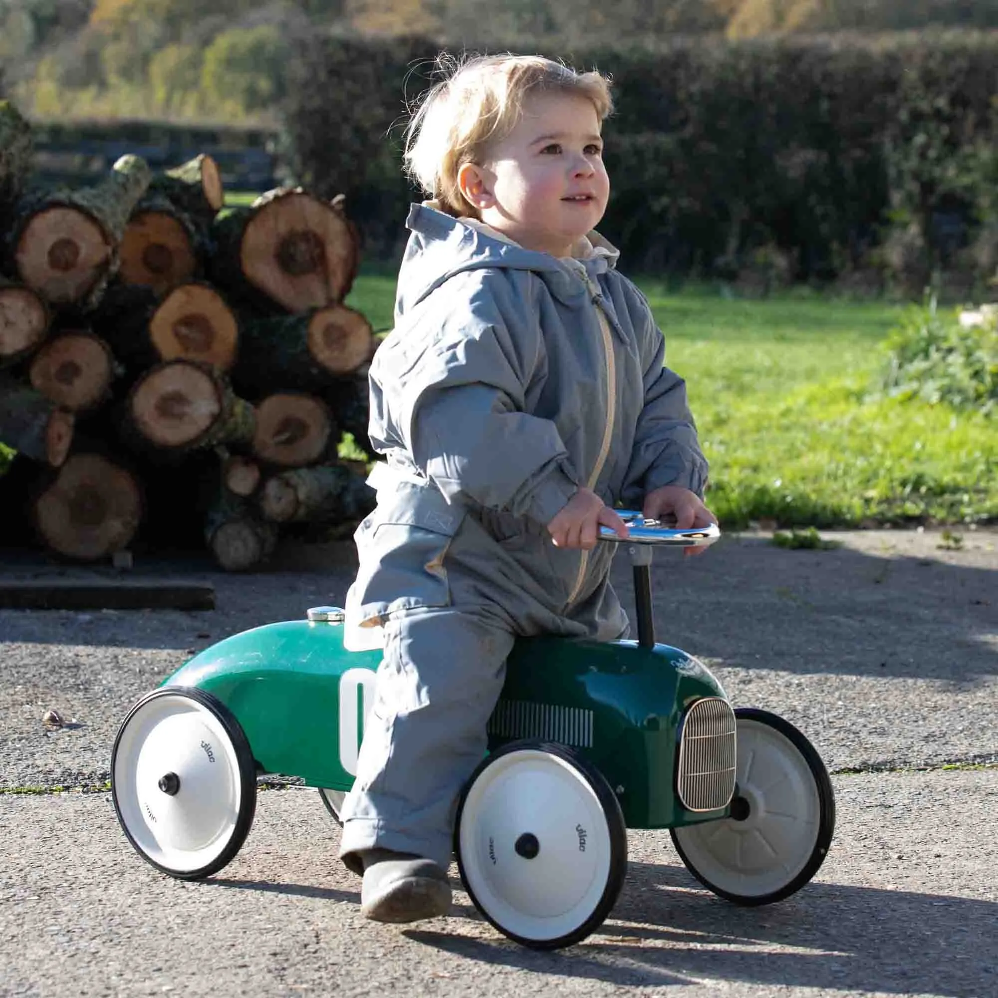 Boy riding the Vilac Classic Car Racing Green in front of log pile
