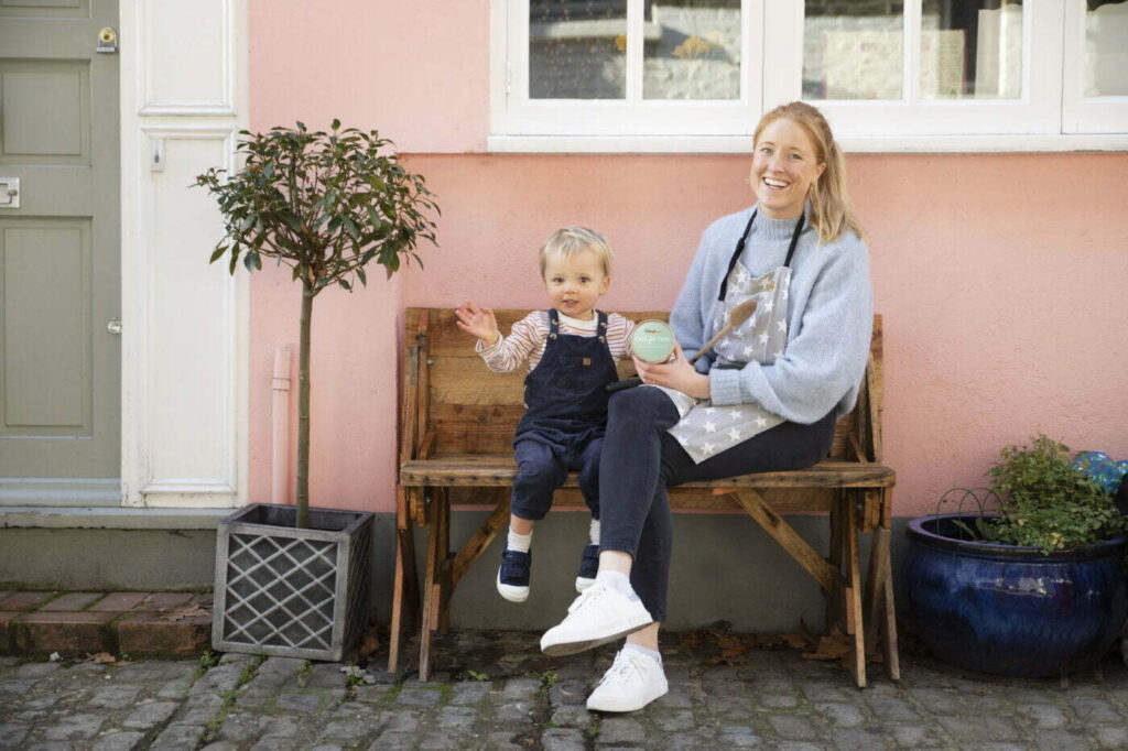A little boy and his mum sat on a wooden bench in front of a pink wall