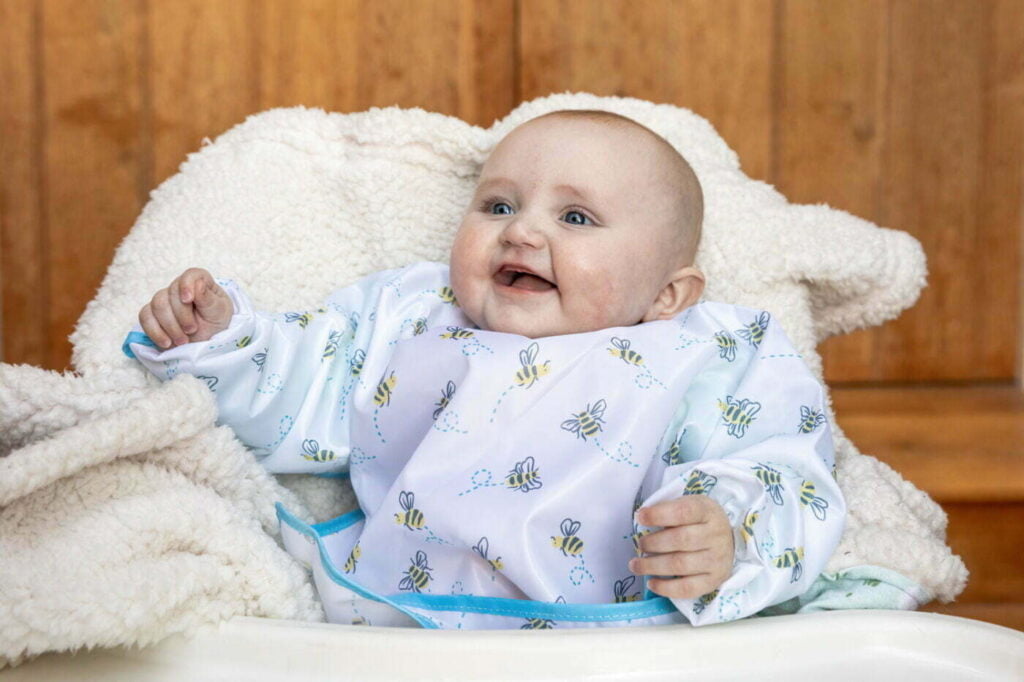 A baby girl laughing whilst wearing a white sleeved baby bib 