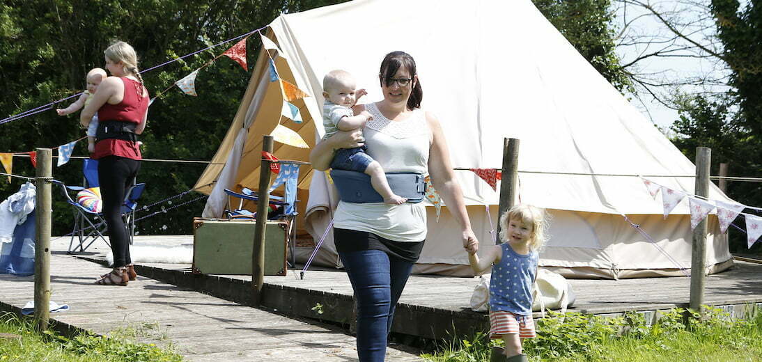 Two ladies with hipseats and young children with tent and bunting behind