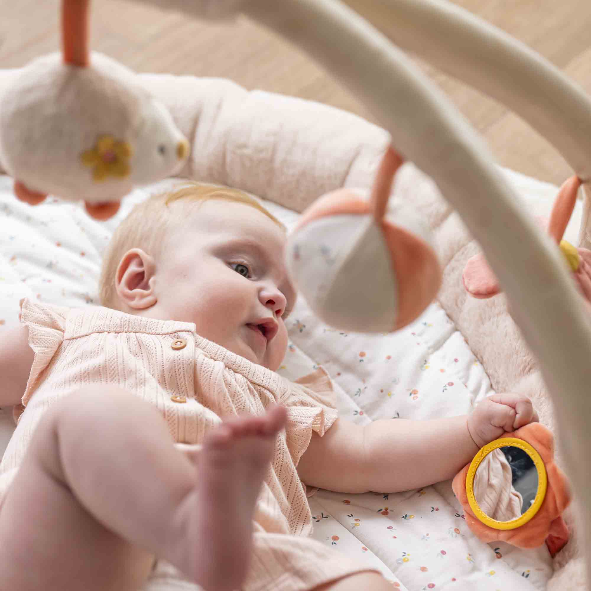 Zoomed in shot of a baby lying on their back playing with the playmat toys