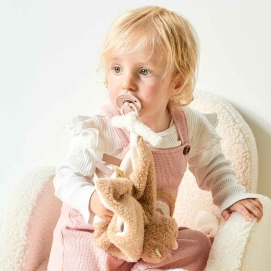 Baby holding Rhino Doudou with pacifier tied to it