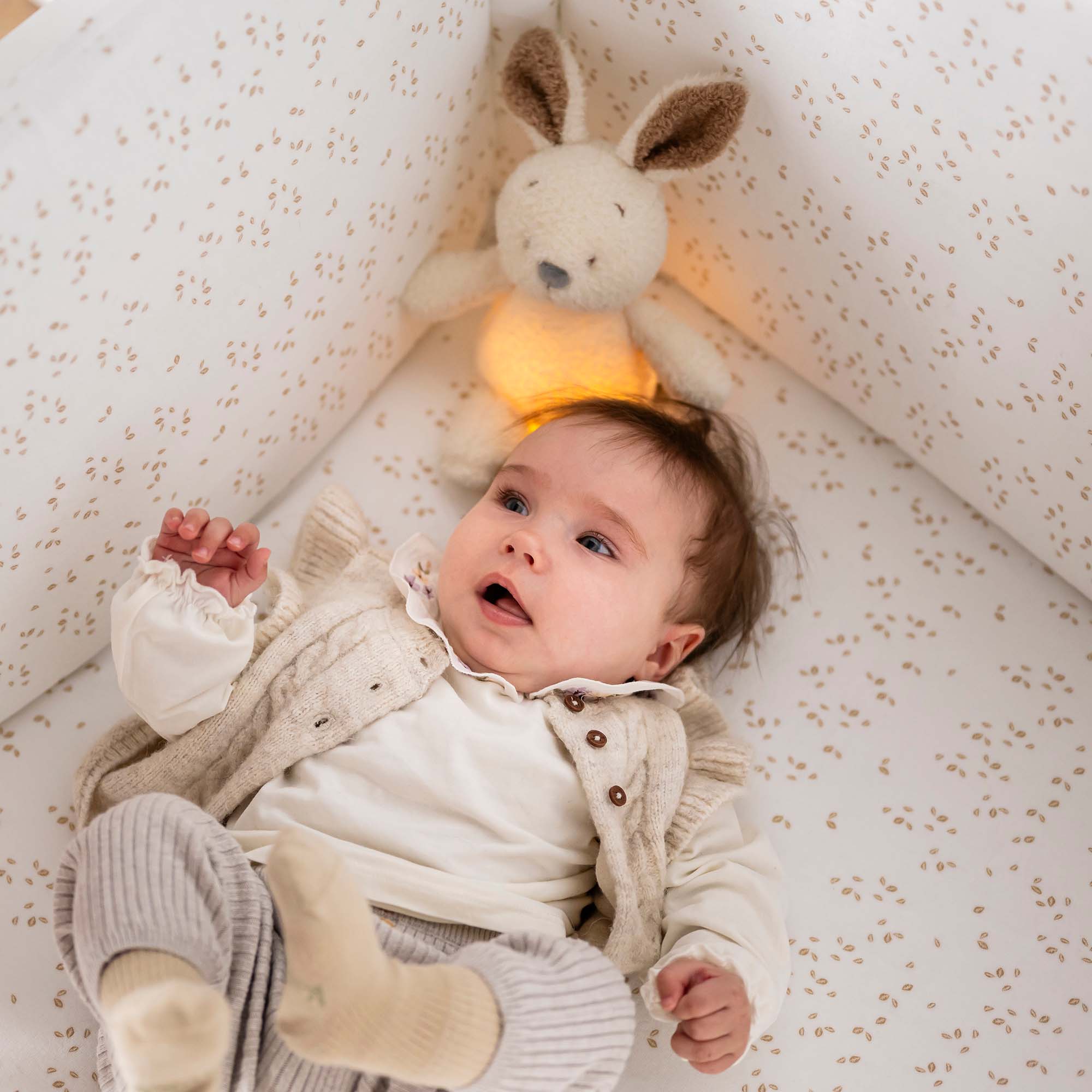 Bunny Cuddly Nightlight sat behind baby in the crib