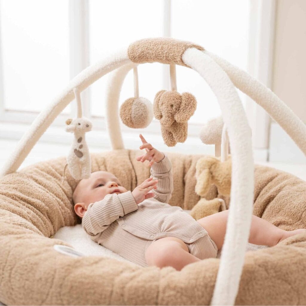 Baby lying on the Nattou Teddy Playmat reaching for the hanging toys
