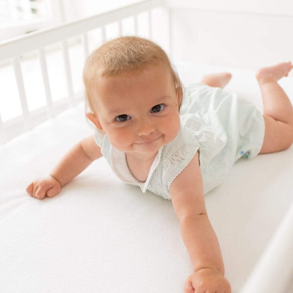 Baby lying in their cot on a mattress protector
